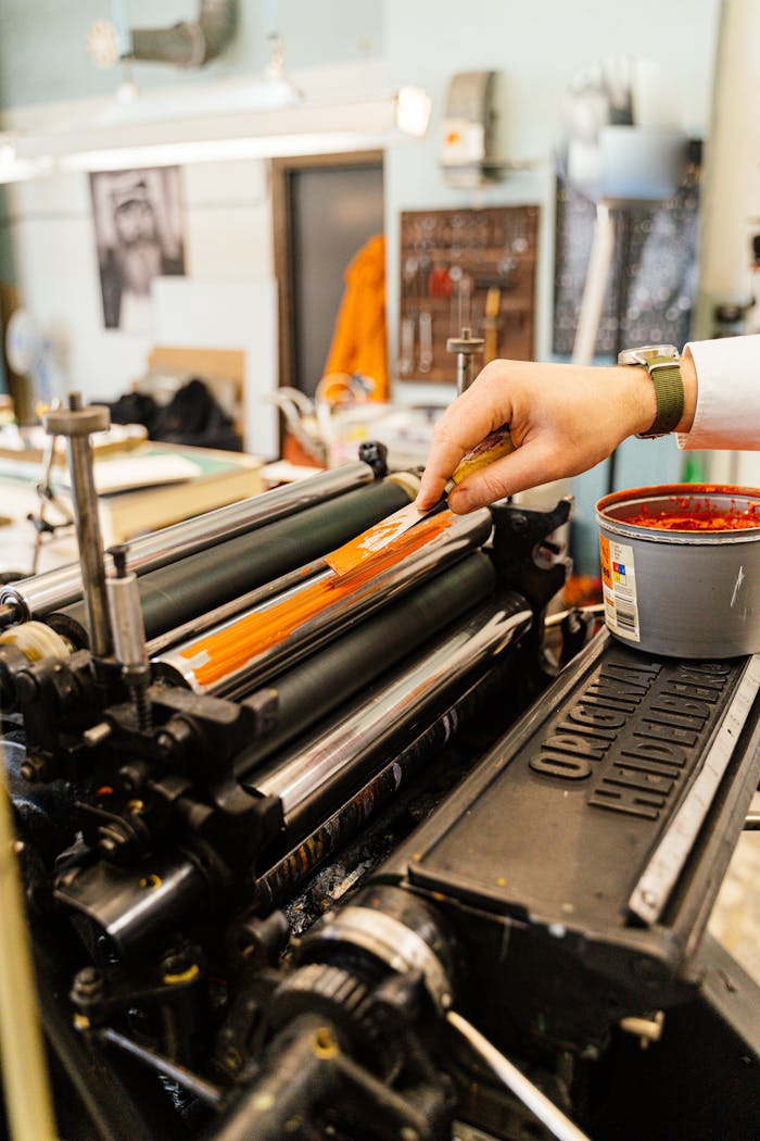 Close-up of a vintage printing press with a hand applying ink, showcasing traditional printing techniques.